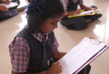 Load image into Gallery viewer, A young Indian girl does math on a clipboard provided by sponsorship