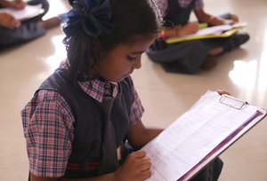 A young Indian girl does math on a clipboard provided by sponsorship
