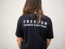 Load image into Gallery viewer, Young woman wearing a black shirt with “100%” on the front to represent our commitment to being a 100% non-profit to fight human trafficking